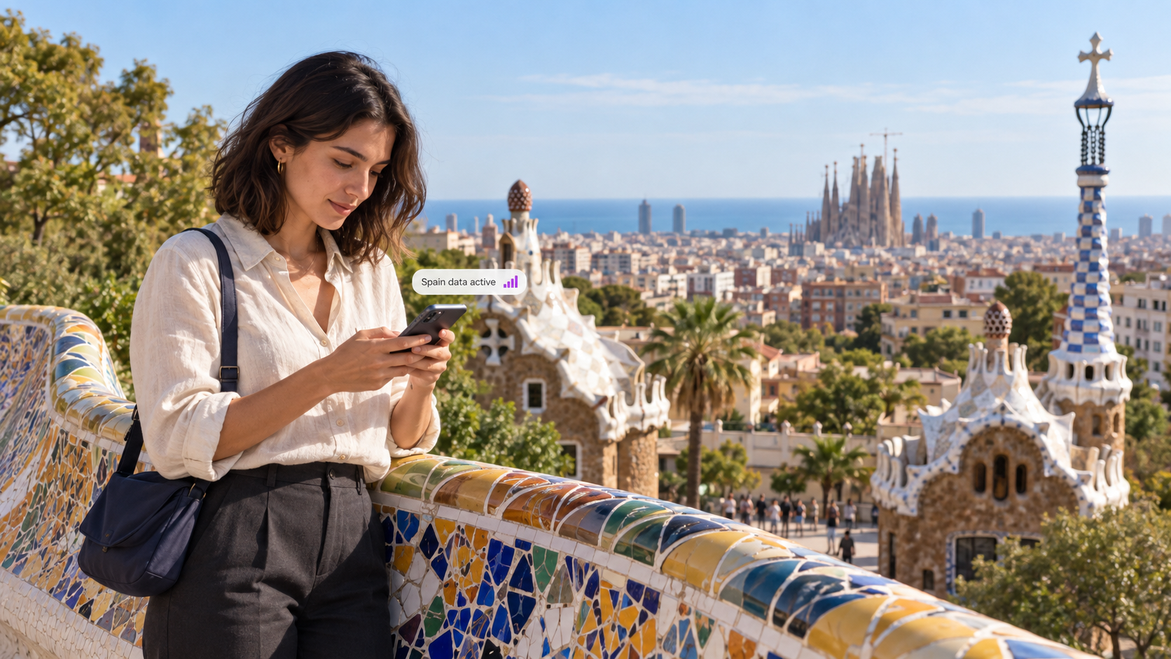 A traveler uses a smartphone at Park Güell in Barcelona, overlooking colorful mosaics and the city skyline, illustrating easy mobile connectivity with a duasim travel eSIM in Spain.