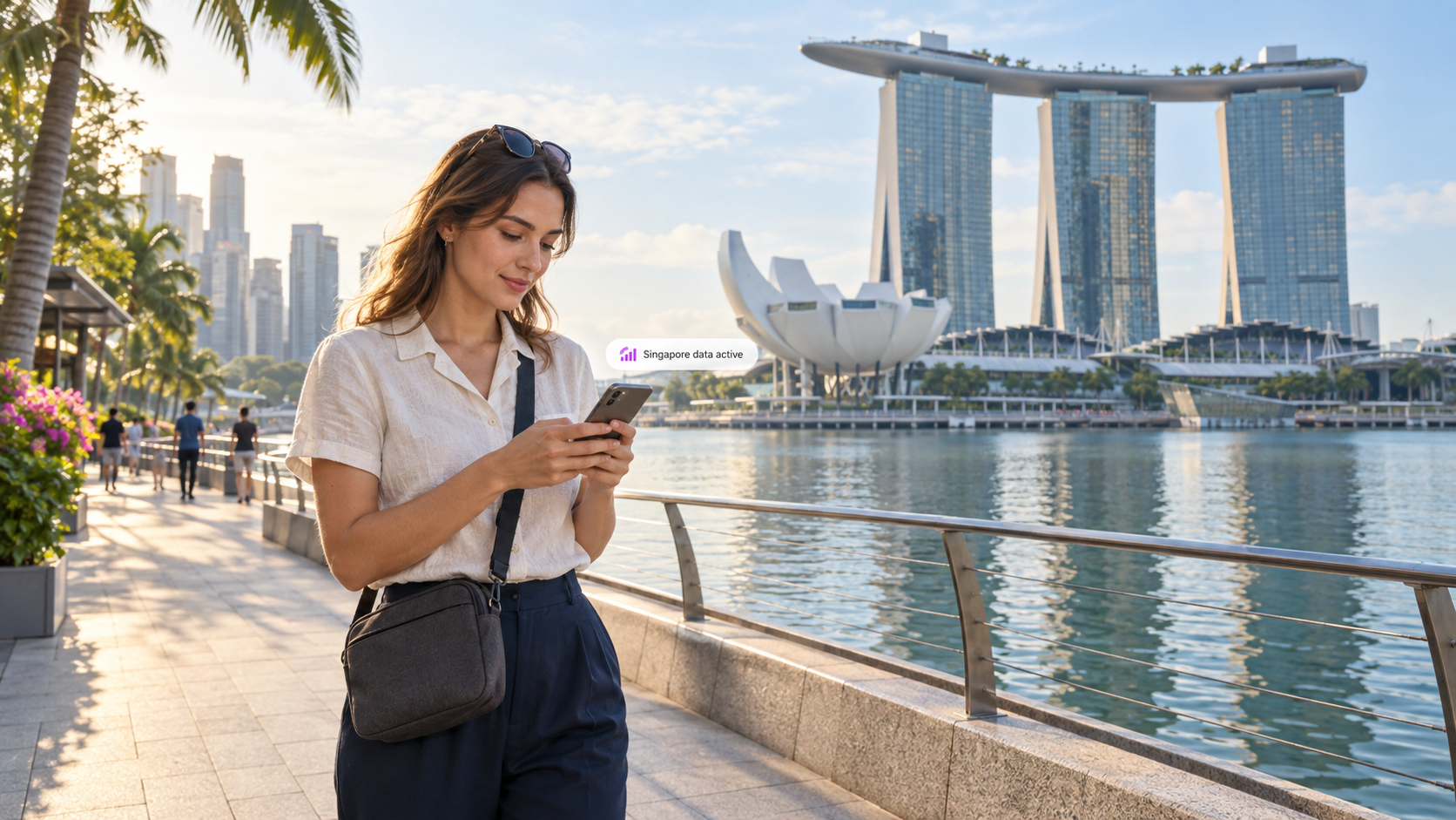 A traveler uses a smartphone beside Singapore’s Marina Bay, with Marina Bay Sands and the ArtScience Museum in the background, illustrating easy mobile connectivity with a duasim travel eSIM.